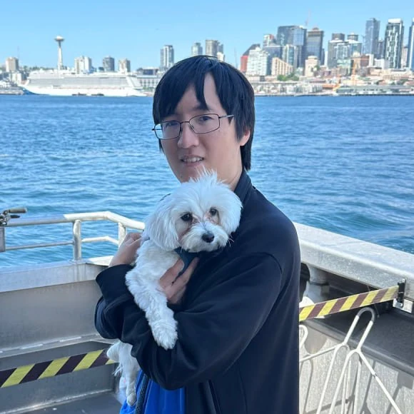 Khoi holding a small white dog on a boat, with Seattle in the background.